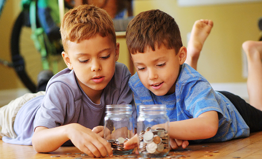 Two young boys counting their money and putting it into money jars