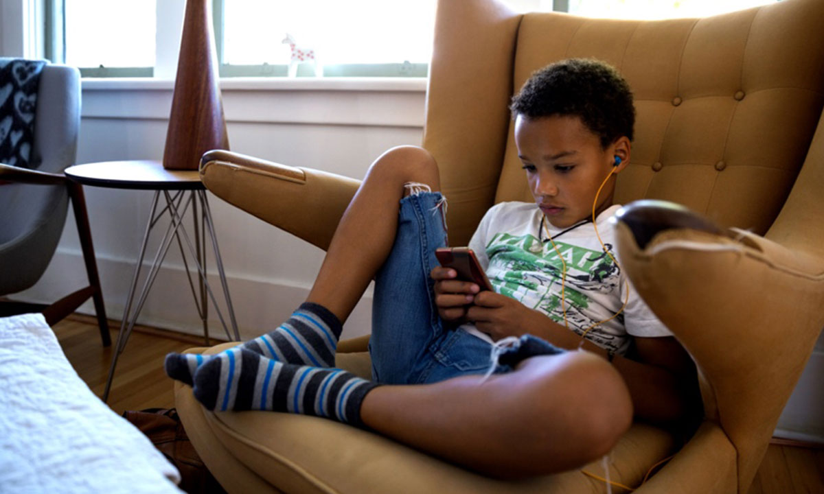 Boy relaxes on a chair wearing headphones and playing on his phone