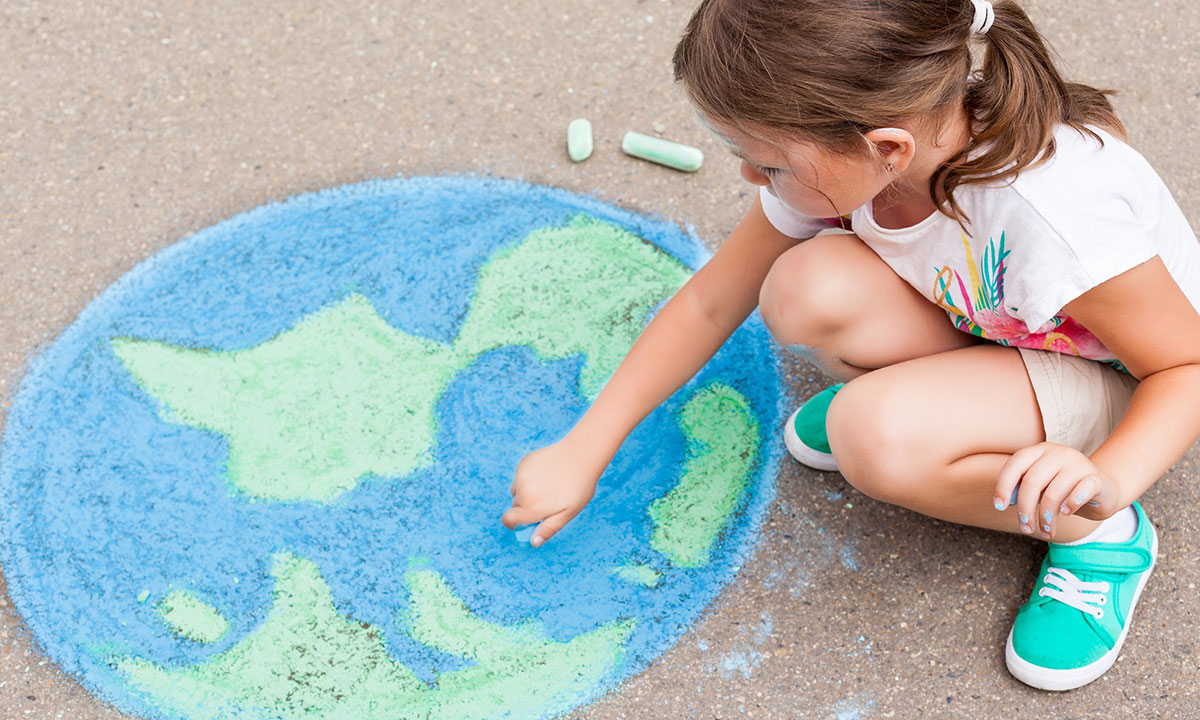 Young girl draws the world with chalk on the ground
