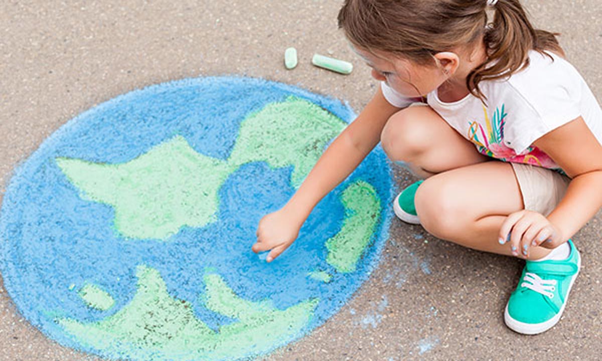 Young girl draws the world with chalk on the ground