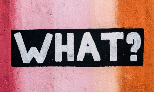 A colourful painted wall with 'WHAT?!' graffitied on it