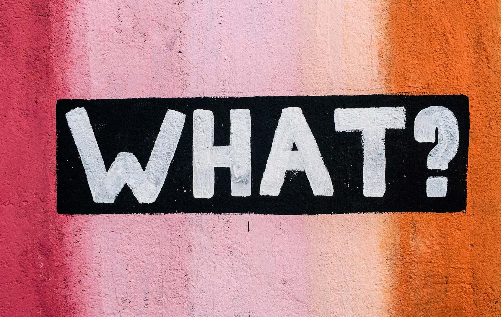 A colourful painted wall with 'WHAT?!' graffitied on it