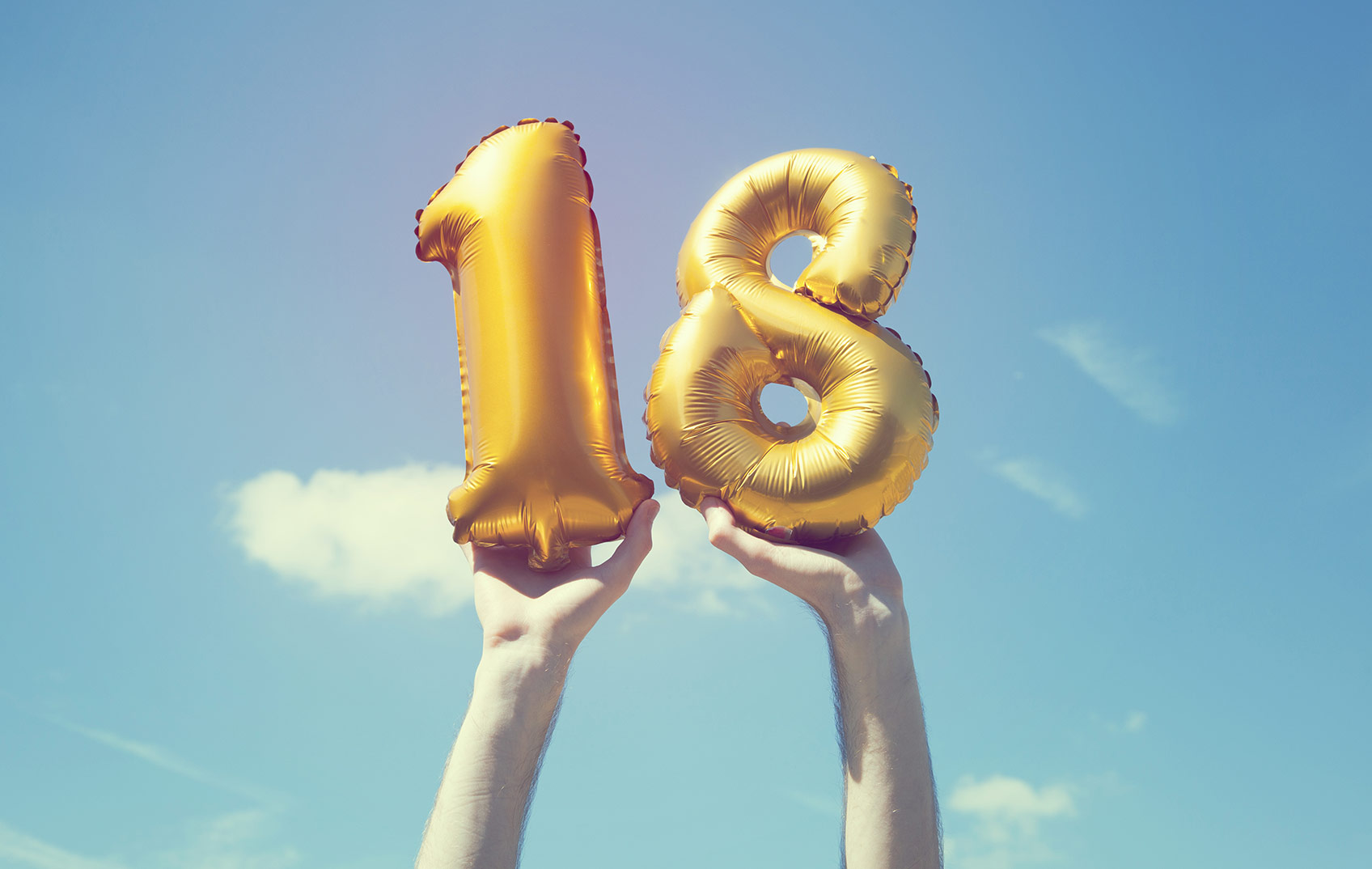 Gold 18th birthday balloons being held in the air 