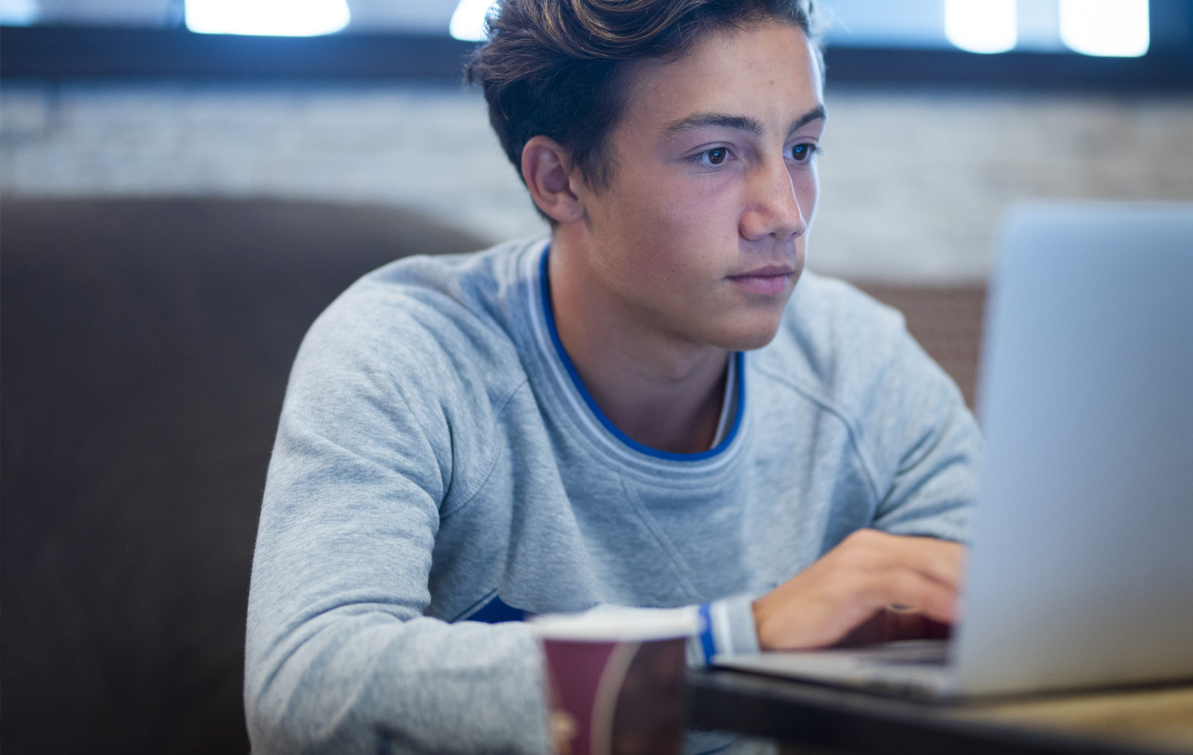 A boy sits working at his laptop in a coffee shop 